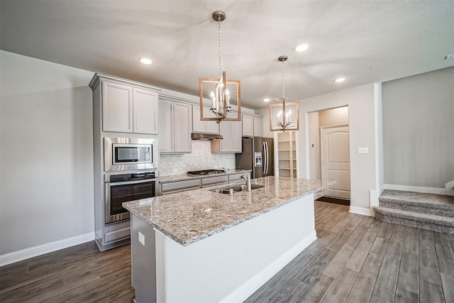 kitchen featuring a sink, a kitchen island with sink, a chandelier, dark wood-style floors, and appliances with stainless steel finishes