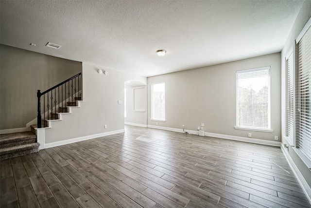 unfurnished living room featuring a textured ceiling, stairway, visible vents, arched walkways, and dark wood-style floors
