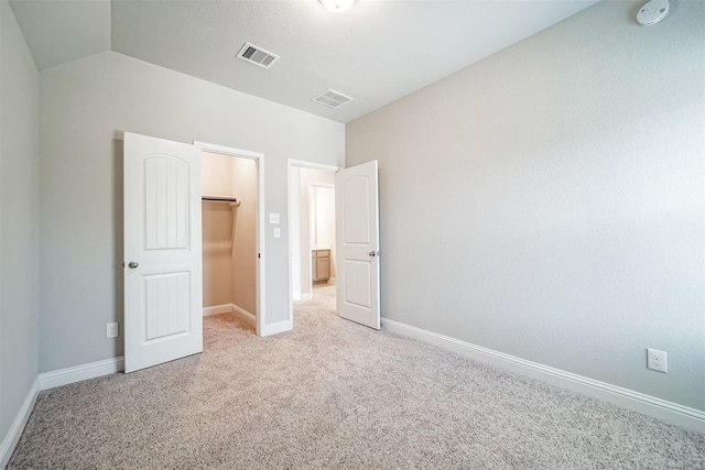 unfurnished bedroom with carpet, visible vents, baseboards, vaulted ceiling, and a spacious closet