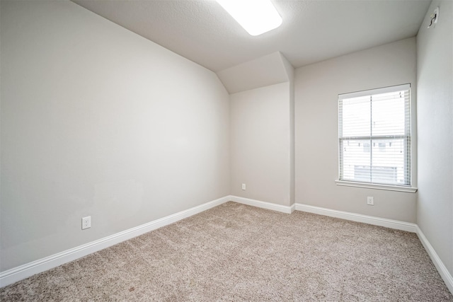 carpeted spare room featuring baseboards and lofted ceiling