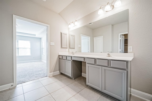 bathroom with a sink, lofted ceiling, tile patterned flooring, double vanity, and baseboards