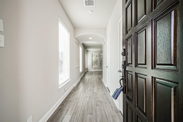 corridor featuring a healthy amount of sunlight, light wood-type flooring, visible vents, baseboards, and arched walkways