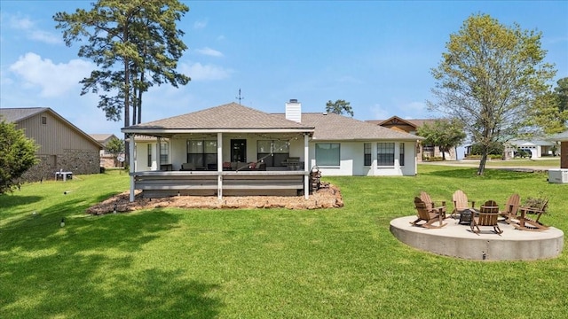 rear view of property featuring a patio, a fire pit, a chimney, a shingled roof, and a yard