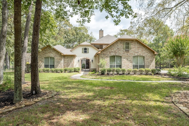 french country home with a front lawn, brick siding, and a chimney