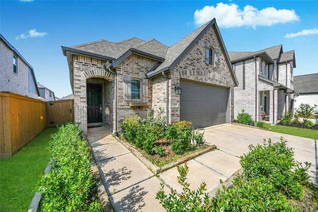french country home with driveway, brick siding, fence, a garage, and stone siding