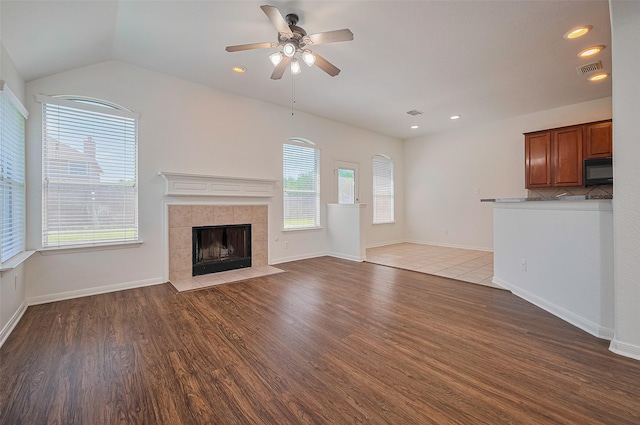 unfurnished living room with a tiled fireplace, wood finished floors, visible vents, and ceiling fan