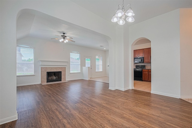 unfurnished living room with wood finished floors, ceiling fan with notable chandelier, a tiled fireplace, baseboards, and vaulted ceiling