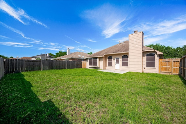 rear view of house with a yard, a chimney, and a fenced backyard