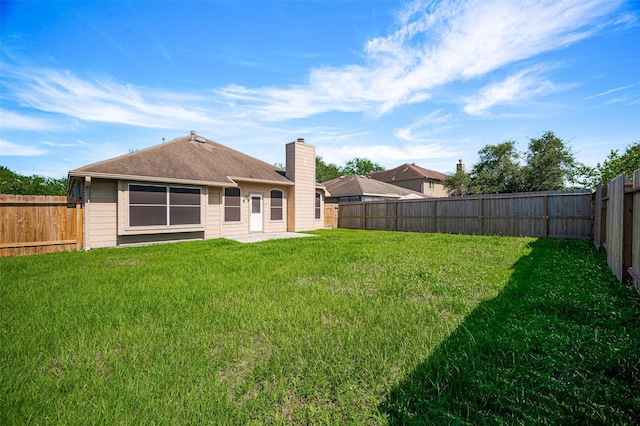 back of house featuring a lawn, a chimney, and a fenced backyard