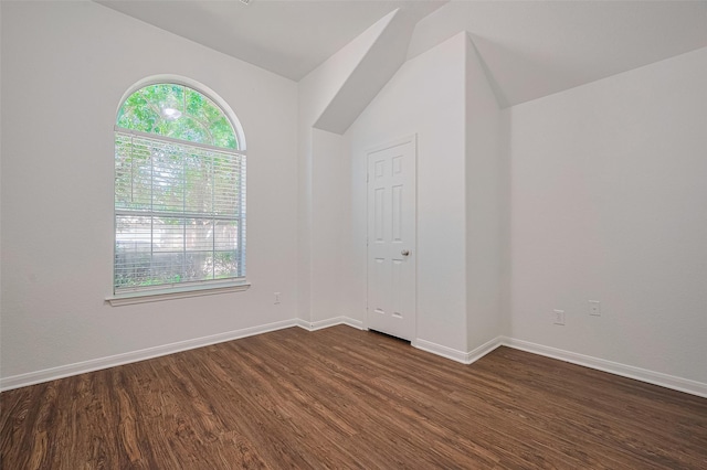 spare room featuring baseboards, vaulted ceiling, plenty of natural light, and dark wood-type flooring
