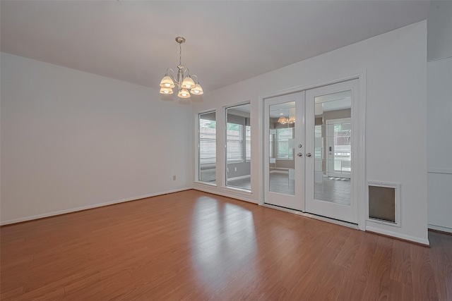 spare room featuring an inviting chandelier, baseboards, french doors, and wood finished floors