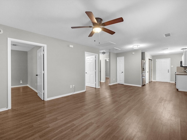 unfurnished living room with attic access, visible vents, dark wood-style flooring, a ceiling fan, and baseboards