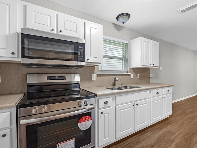 kitchen with a sink, white cabinetry, dark wood-type flooring, light countertops, and appliances with stainless steel finishes