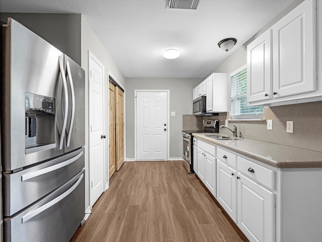 kitchen with white cabinets, stainless steel appliances, wood finished floors, and a sink