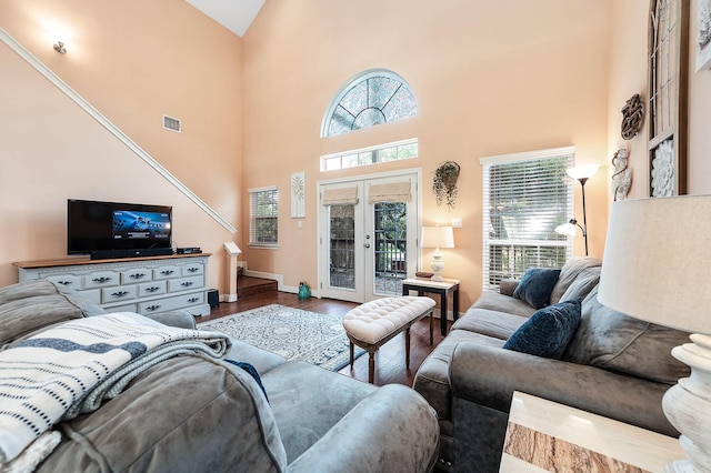 living area with a towering ceiling, visible vents, plenty of natural light, and wood finished floors