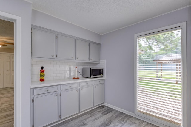 150 County Road 146, Alvin, TX 77511 - kitchen with stainless steel microwave, a textured ceiling, light wood-style flooring, decorative backsplash, and light countertops