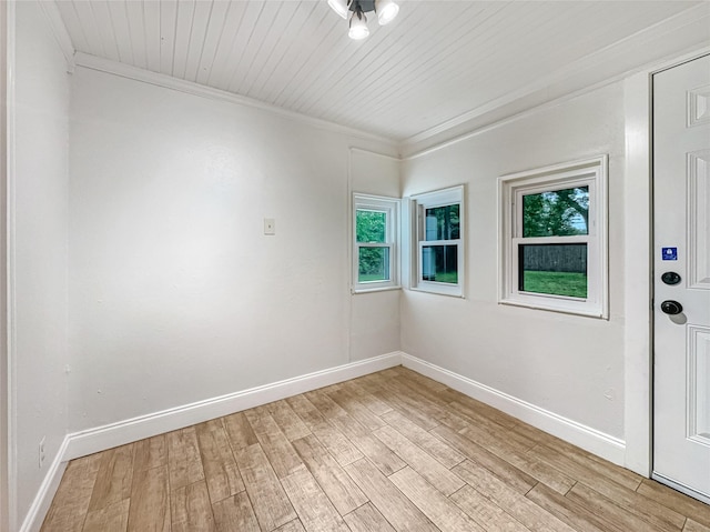 empty room with ornamental molding, a wealth of natural light, baseboards, and light wood-type flooring