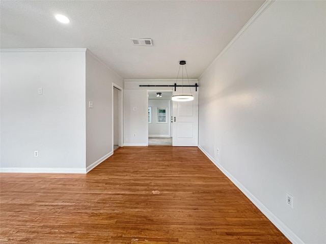spare room with wood finished floors, visible vents, a barn door, baseboards, and ornamental molding