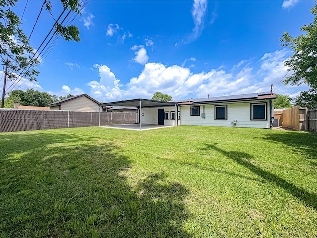 rear view of house featuring roof mounted solar panels, a patio area, a lawn, and a fenced backyard