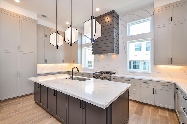 4709 Gibson St, Houston, TX 77007 - kitchen featuring stove, wall chimney exhaust hood, a kitchen island with sink, tasteful backsplash, and light wood finished floors