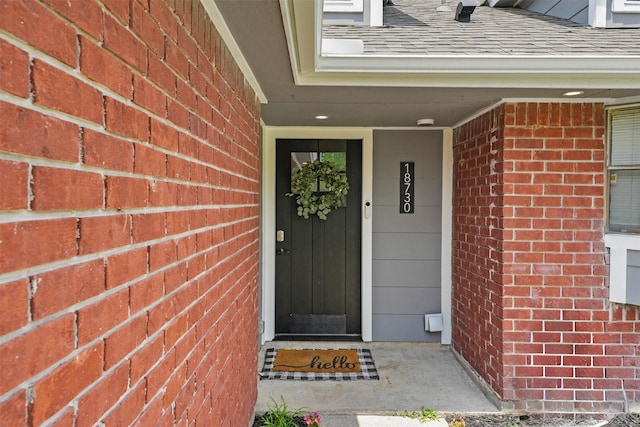 entrance to property with a shingled roof and brick siding