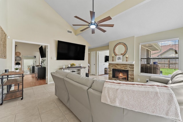 living room featuring high vaulted ceiling, visible vents, ceiling fan, light tile patterned floors, and a stone fireplace