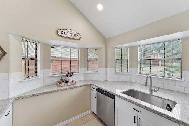 kitchen featuring a sink, light tile patterned flooring, white cabinetry, stainless steel dishwasher, and light stone countertops