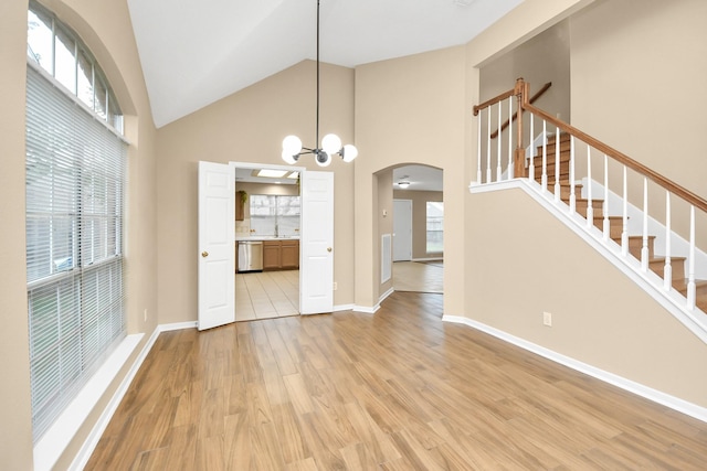unfurnished dining area featuring high vaulted ceiling, light wood-type flooring, baseboards, arched walkways, and stairs