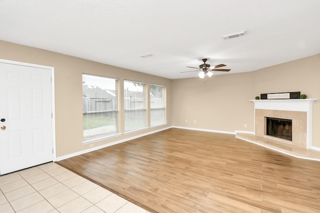 unfurnished living room featuring a ceiling fan, light wood-style floors, a tiled fireplace, and visible vents