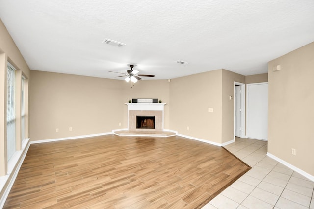 unfurnished living room with a ceiling fan, a fireplace with raised hearth, baseboards, visible vents, and light wood-style floors