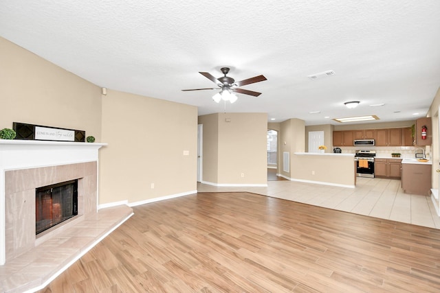 unfurnished living room with a tile fireplace, a textured ceiling, ceiling fan, visible vents, and light wood-style floors