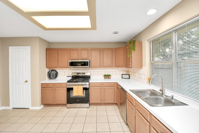 kitchen with a sink, stainless steel appliances, light brown cabinetry, light countertops, and decorative backsplash