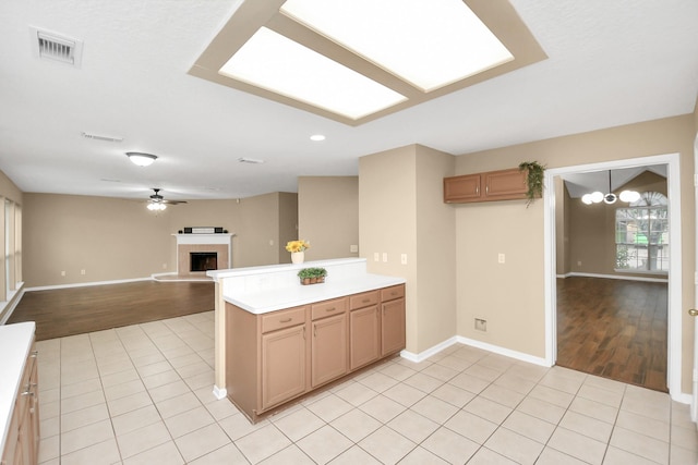 kitchen with light wood finished floors, a tiled fireplace, visible vents, baseboards, and light countertops