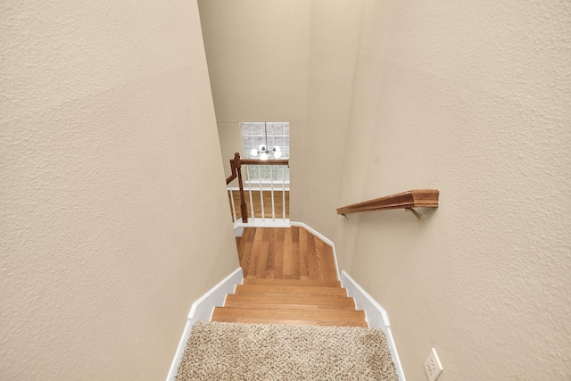 stairway featuring baseboards, a textured wall, and wood finished floors
