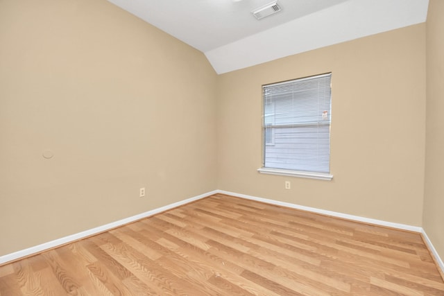 spare room with vaulted ceiling, light wood-style floors, visible vents, and baseboards