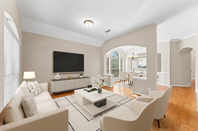 living room with a notable chandelier, light wood-style flooring, visible vents, vaulted ceiling, and arched walkways