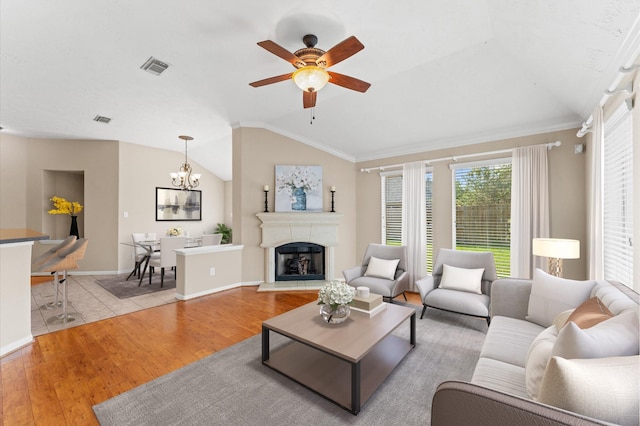living room featuring ceiling fan with notable chandelier, wood finished floors, visible vents, and vaulted ceiling