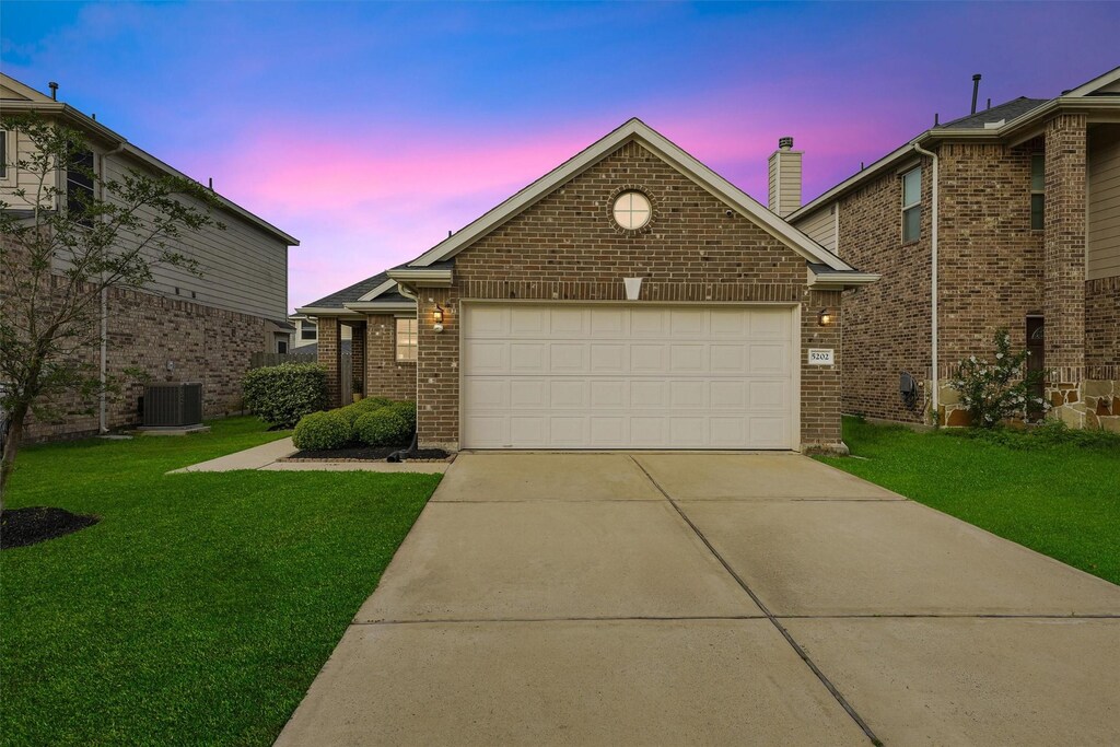 view of front of home featuring driveway, brick siding, a garage, central AC, and a front lawn
