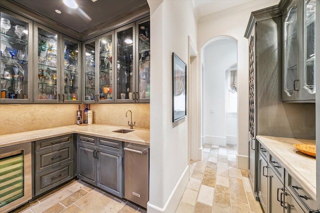 bar with beverage cooler, a sink, baseboards, arched walkways, and wet bar
