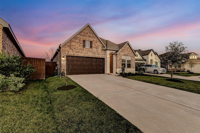 french country home featuring concrete driveway, brick siding, a front lawn, and fence