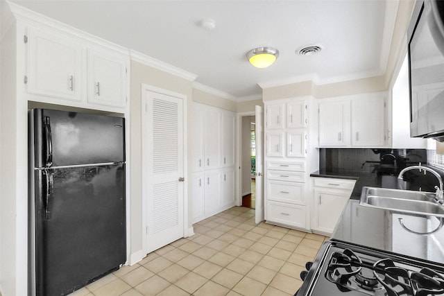 kitchen featuring freestanding refrigerator, a sink, gas stove, white cabinets, and ornamental molding