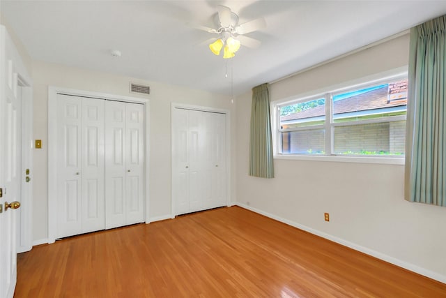 unfurnished bedroom featuring light wood finished floors, baseboards, multiple closets, and a ceiling fan