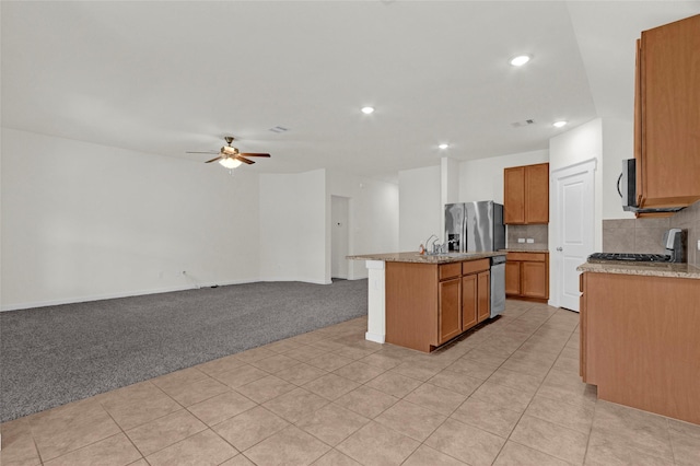 kitchen featuring a ceiling fan, an island with sink, stainless steel appliances, light carpet, and recessed lighting