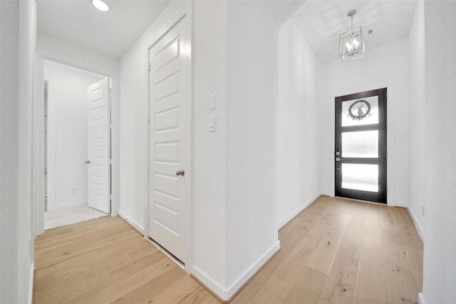 entryway with baseboards, light wood finished floors, and a chandelier