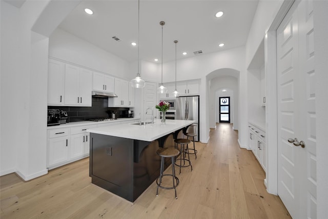 kitchen with freestanding refrigerator, light wood finished floors, visible vents, a sink, and arched walkways
