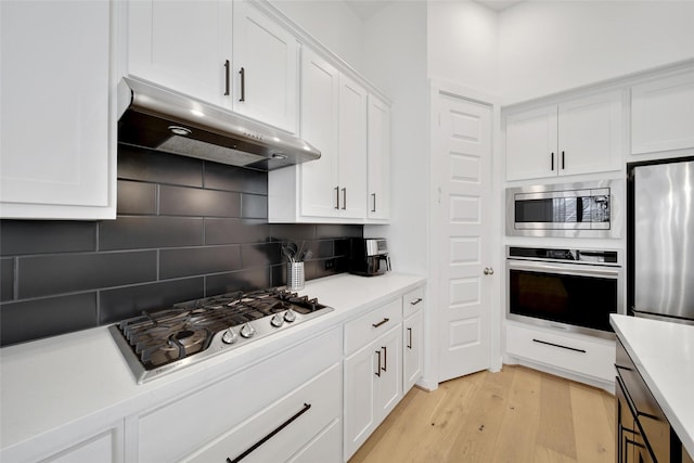 kitchen featuring stainless steel appliances, light wood-type flooring, under cabinet range hood, backsplash, and white cabinets