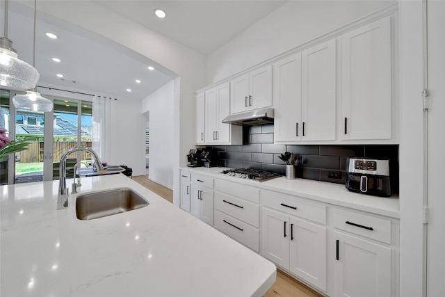 kitchen with a sink, tasteful backsplash, recessed lighting, under cabinet range hood, and white cabinetry
