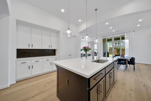 kitchen with a sink, light wood finished floors, dark brown cabinetry, decorative backsplash, and light countertops