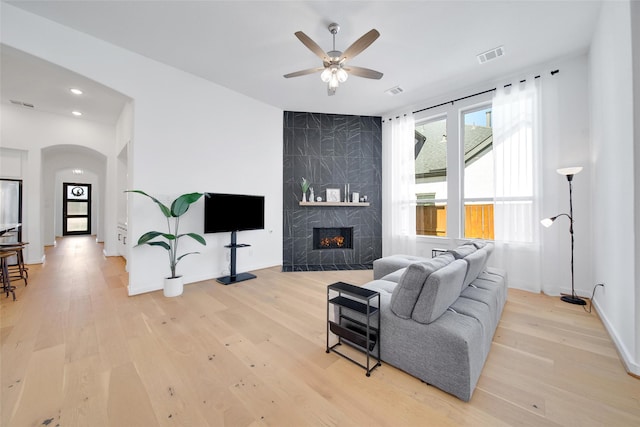 living area with a ceiling fan, light wood finished floors, visible vents, arched walkways, and a fireplace