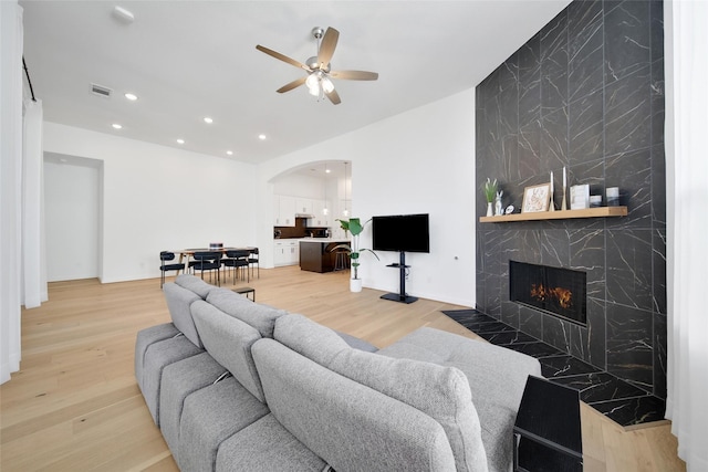 living room with light wood-type flooring, visible vents, ceiling fan, a large fireplace, and arched walkways